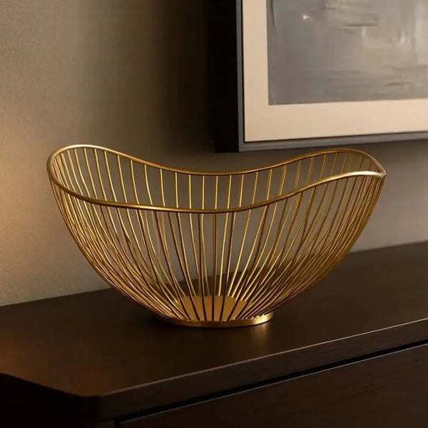 Fruteira Royale Casavelle dourada em metal sobre aparador escuro, com design escultural e curvas elegantes em ambiente sofisticado.