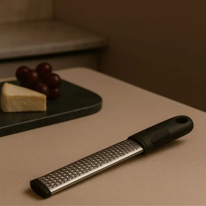 Ralador de queijo Maestro Casavelle sobre bancada bege com pedaço de queijo e uvas ao fundo em ambiente sofisticado.