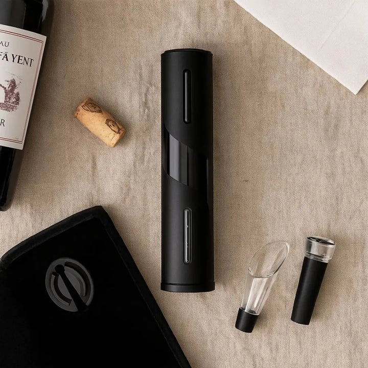 Abridor de vinho elétrico premium em acabamento preto fosco sobre tecido beige, acompanhado de rolha, bico dosador e tampa a vácuo, com garrafa de vinho em destaque parcial – composição minimalista e sofisticada.